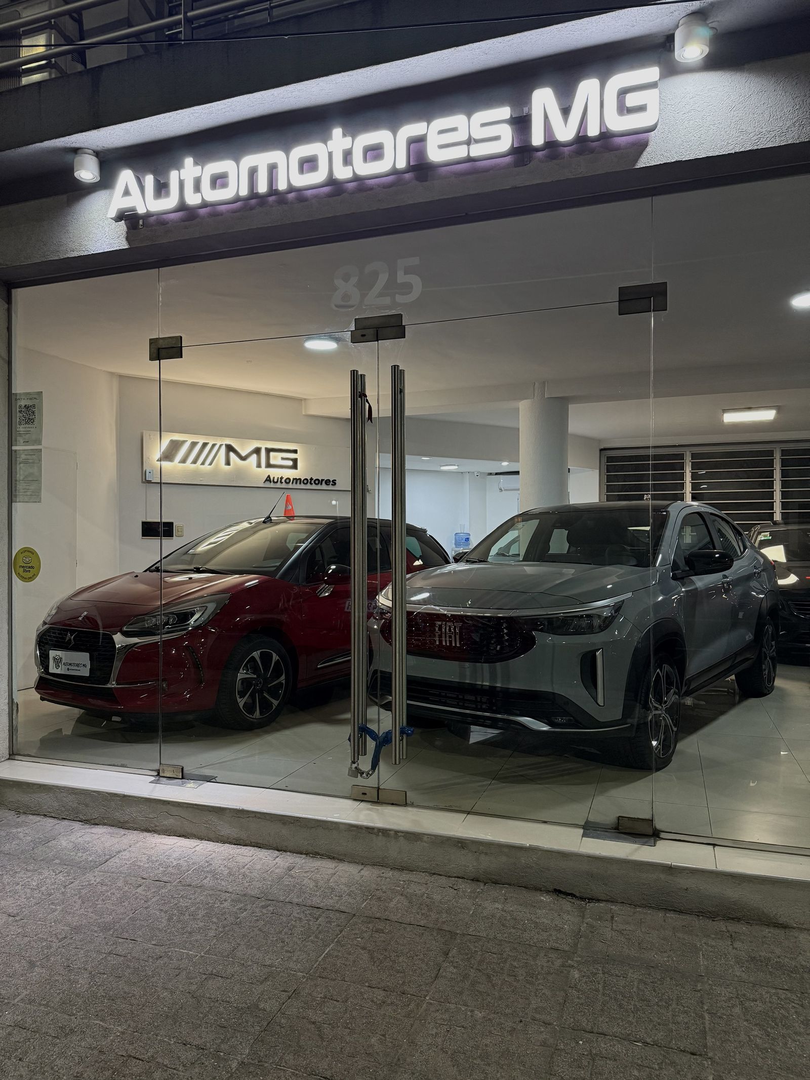 Frente del local de Automotores MG de noche, con autos en exhibición